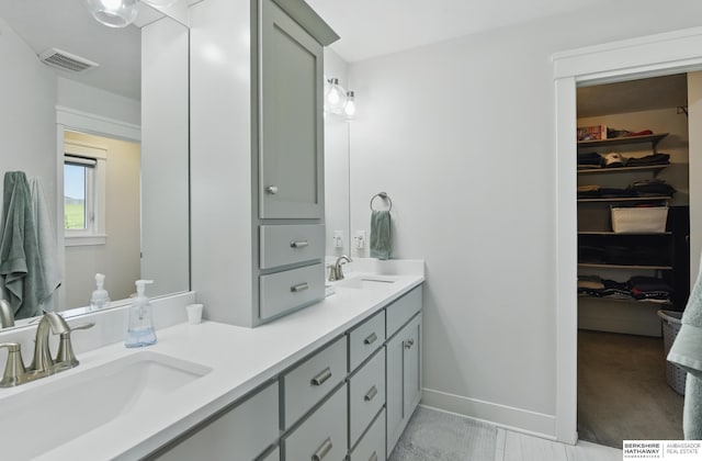 full bathroom featuring double vanity, a spacious closet, and baseboards