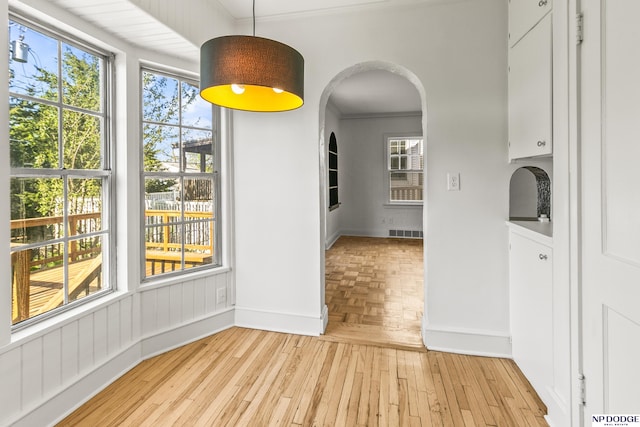 unfurnished dining area featuring crown molding, baseboards, arched walkways, and light wood finished floors