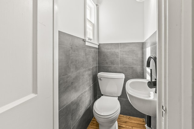 half bathroom featuring wood finished floors, tile walls, toilet, and a wainscoted wall