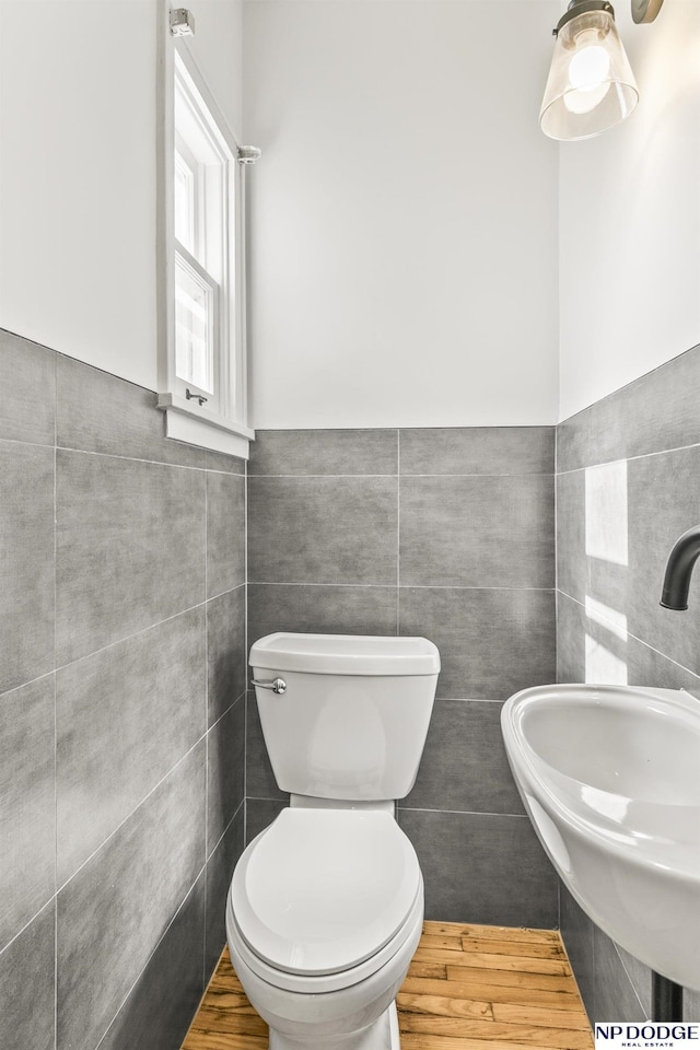 half bath with tile walls, a sink, toilet, and a wainscoted wall