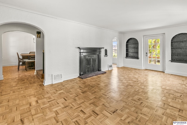 unfurnished living room featuring arched walkways, baseboards, a fireplace, and crown molding