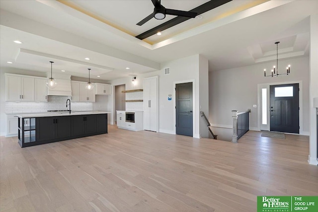kitchen featuring a tray ceiling, white cabinets, decorative backsplash, light countertops, and light wood finished floors