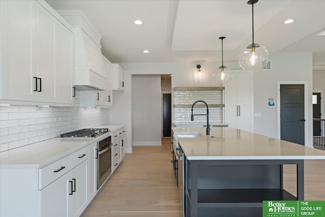 kitchen featuring a sink, stainless steel appliances, backsplash, light wood-style flooring, and light countertops