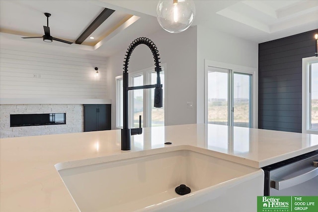 detailed view of a tray ceiling, a ceiling fan, a fireplace, wood walls, and dishwasher