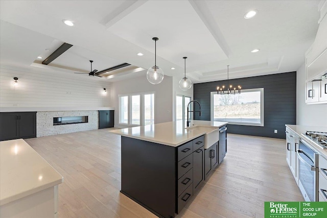 kitchen with a tray ceiling, a sink, light countertops, a stone fireplace, and recessed lighting