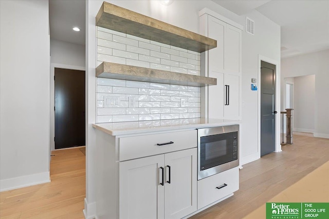 kitchen featuring built in microwave, light wood-style floors, light countertops, white cabinets, and baseboards