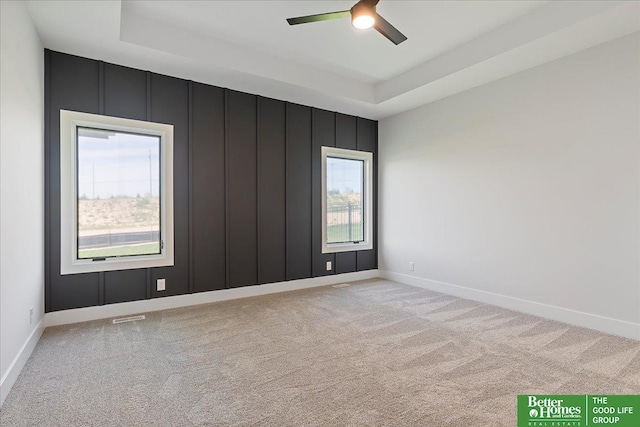 unfurnished room with light carpet, a ceiling fan, a tray ceiling, and baseboards