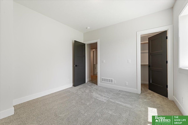 unfurnished bedroom featuring a walk in closet, light colored carpet, baseboards, and a closet