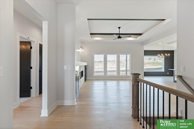 corridor with a tray ceiling, a chandelier, an upstairs landing, light wood-type flooring, and baseboards
