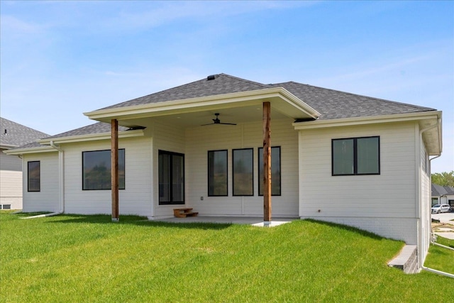 back of house featuring roof with shingles, a lawn, and a ceiling fan