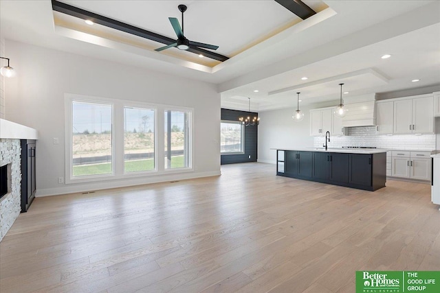 unfurnished living room featuring a tray ceiling, a chandelier, a fireplace, a sink, and light wood-type flooring