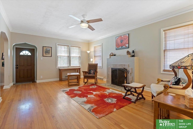 living area featuring arched walkways, light wood finished floors, a ceiling fan, crown molding, and a tile fireplace