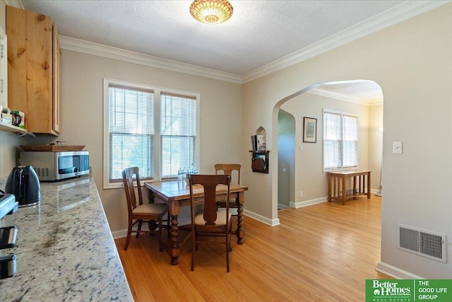 dining room with arched walkways, light wood-style floors, crown molding, and baseboards
