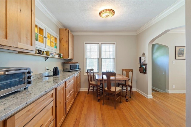 kitchen featuring stainless steel microwave, arched walkways, light wood-style floors, ornamental molding, and baseboards