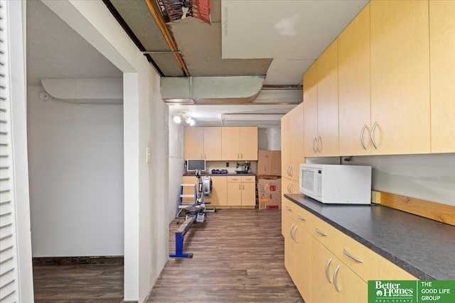 kitchen featuring white microwave, dark wood-type flooring, dark countertops, and light brown cabinetry