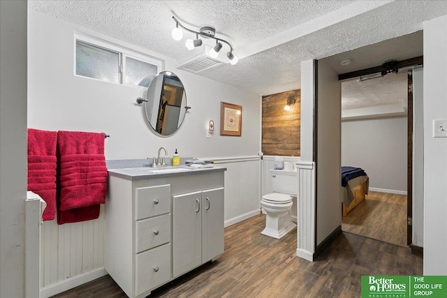bathroom with toilet, wood finished floors, vanity, a textured ceiling, and a wainscoted wall