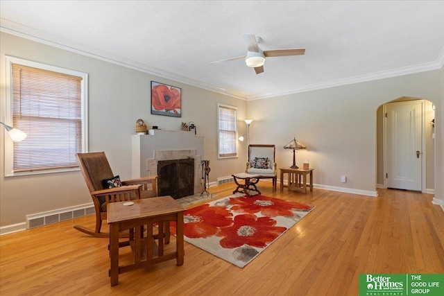 living room with a fireplace with flush hearth, wood finished floors, a ceiling fan, crown molding, and arched walkways