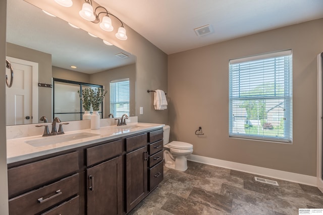 bathroom featuring baseboards, a shower with shower door, double vanity, toilet, and stone finish floors