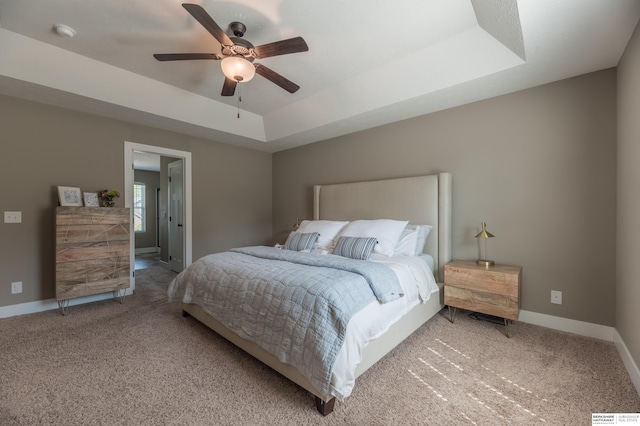 bedroom with carpet floors, a raised ceiling, baseboards, and a ceiling fan