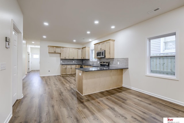 kitchen featuring stainless steel appliances, a peninsula, dark countertops, a sink, and backsplash