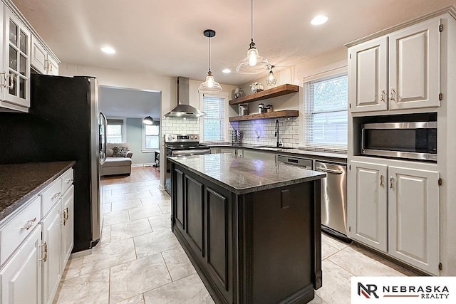 kitchen featuring wall chimney range hood, stainless steel appliances, a sink, backsplash, and a kitchen island