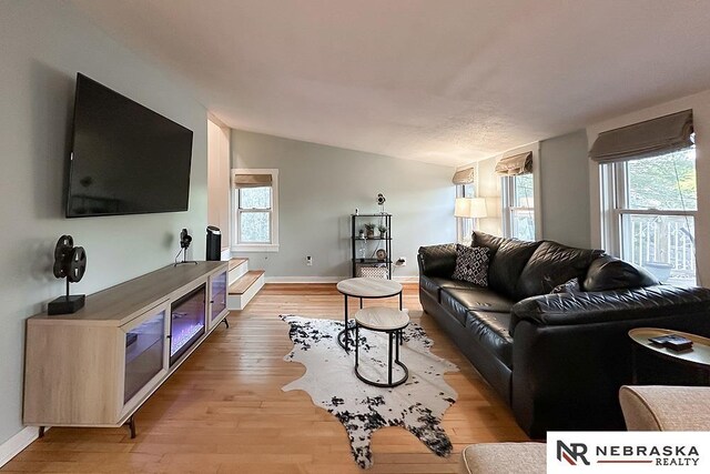 living area featuring lofted ceiling, light wood-style floors, and baseboards