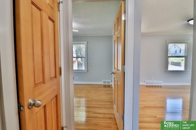 hallway featuring light wood-type flooring, ornamental molding, and baseboards