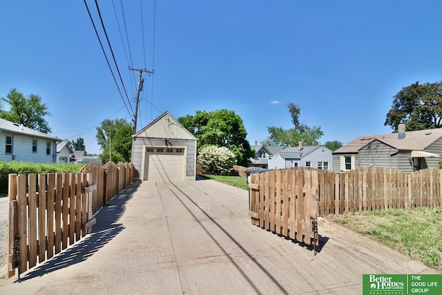 view of front of property with concrete driveway, fence, an outdoor structure, a detached garage, and a residential view
