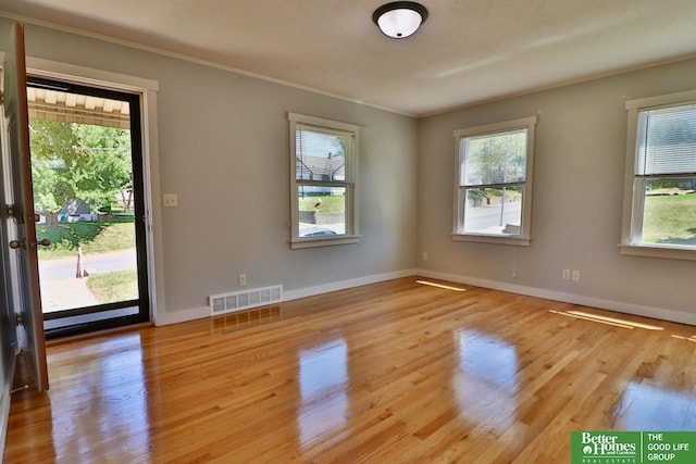 empty room featuring plenty of natural light, wood finished floors, ornamental molding, and baseboards