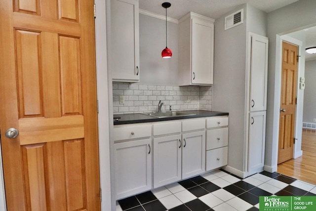 kitchen featuring a sink, dark countertops, white cabinets, decorative backsplash, and pendant lighting