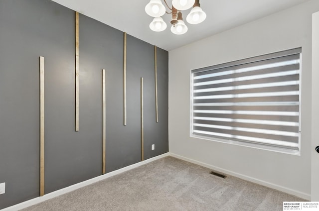 carpeted empty room featuring a chandelier and baseboards