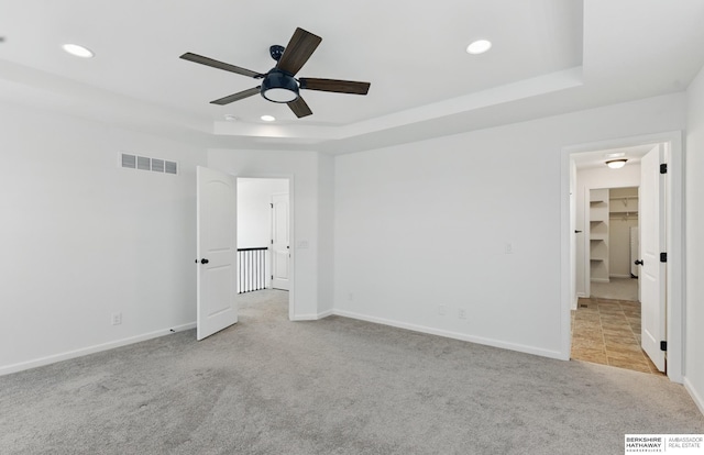 empty room with a tray ceiling, a ceiling fan, carpet flooring, recessed lighting, and baseboards