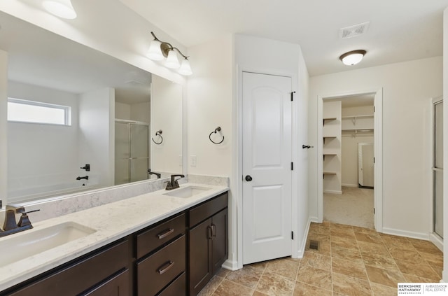 bathroom with a shower stall, double vanity, a walk in closet, and stone finish floors