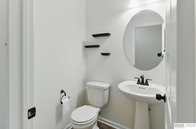 half bathroom with toilet, baseboards, and a sink