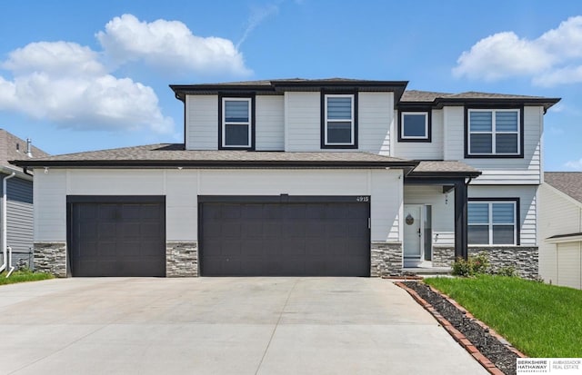 prairie-style home featuring driveway, stone siding, and a garage