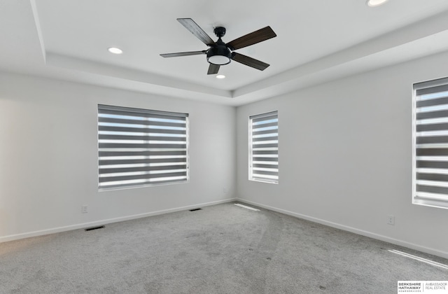carpeted spare room with a raised ceiling, recessed lighting, ceiling fan, and baseboards