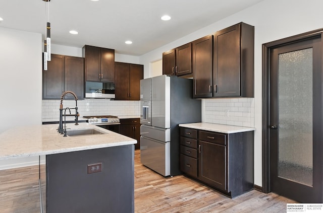 kitchen with white microwave, stainless steel fridge, dark brown cabinets, a sink, and light wood-type flooring