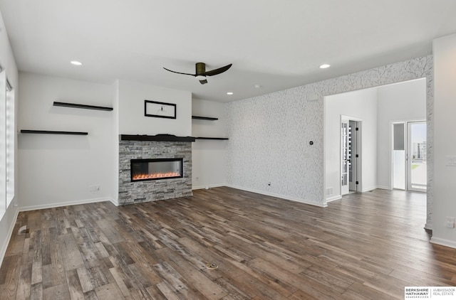 unfurnished living room featuring a ceiling fan, dark wood-type flooring, a stone fireplace, recessed lighting, and baseboards