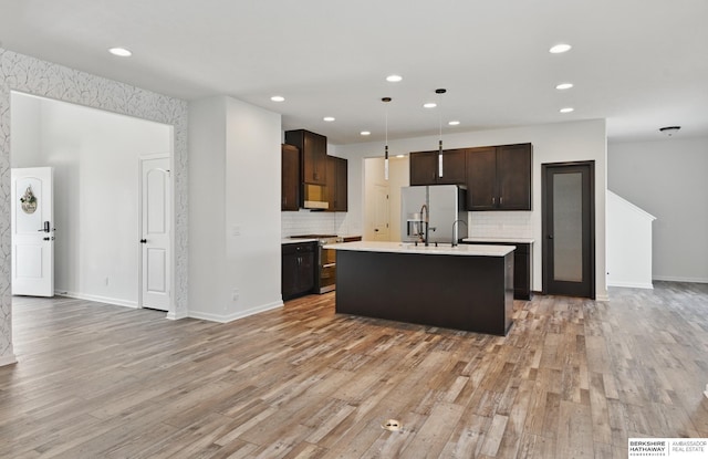 kitchen featuring appliances with stainless steel finishes, light countertops, dark brown cabinets, light wood-type flooring, and tasteful backsplash