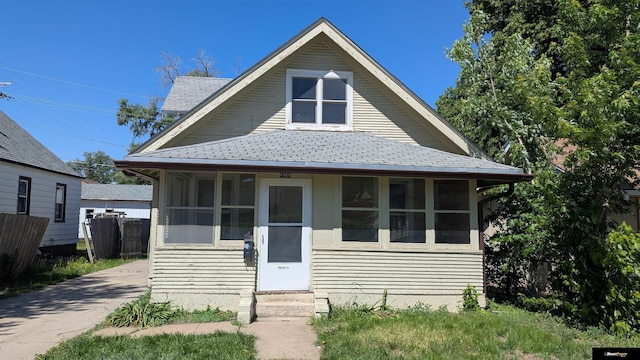 view of front of property with a shingled roof, a sunroom, and fence