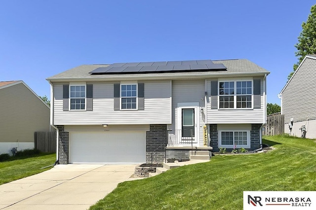 split foyer home featuring concrete driveway, solar panels, and an attached garage