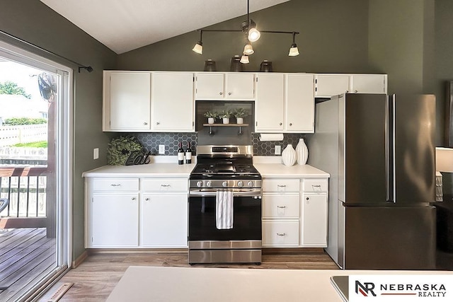 kitchen with appliances with stainless steel finishes, vaulted ceiling, tasteful backsplash, white cabinets, and wood finished floors