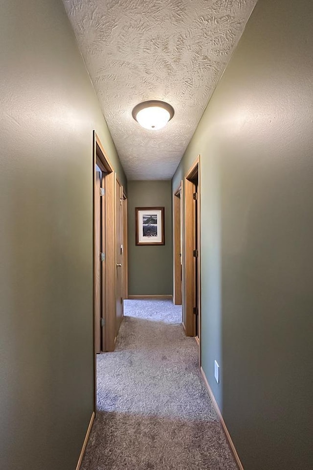 corridor featuring carpet, a textured ceiling, and baseboards