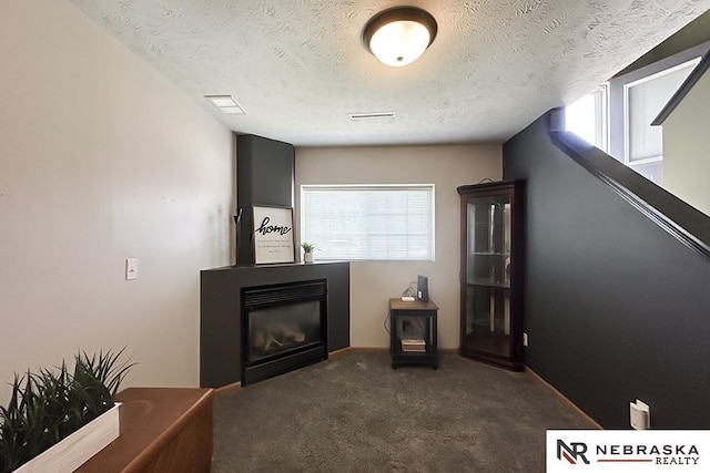 unfurnished room featuring plenty of natural light, a glass covered fireplace, a textured ceiling, dark carpet, and baseboards