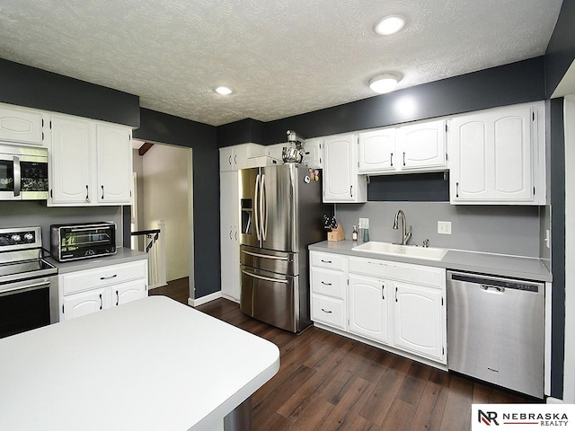 kitchen with appliances with stainless steel finishes, a sink, dark wood-style flooring, white cabinets, and a textured ceiling