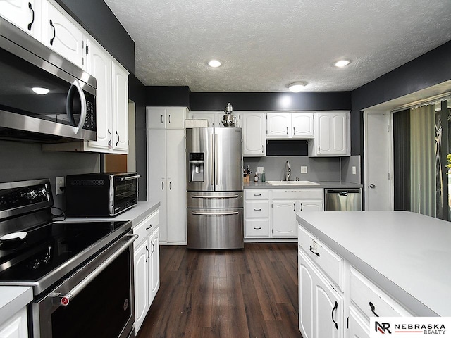 kitchen featuring stainless steel appliances, a sink, light countertops, dark wood finished floors, and white cabinets