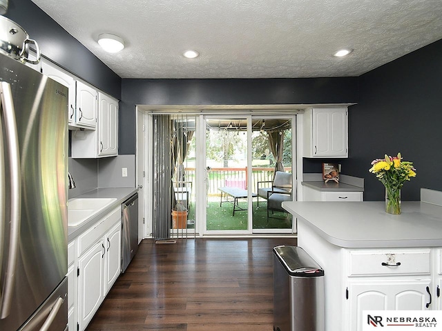 kitchen with appliances with stainless steel finishes, white cabinetry, a textured ceiling, dark wood-style floors, and light countertops