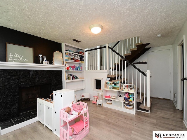 playroom with wood finished floors, a textured ceiling, and a high end fireplace