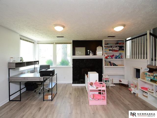 office area featuring a textured ceiling, wood finished floors, a premium fireplace, and baseboards