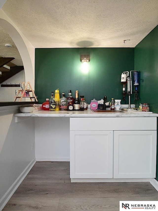 bar area with a textured ceiling, a sink, wood finished floors, and arched walkways
